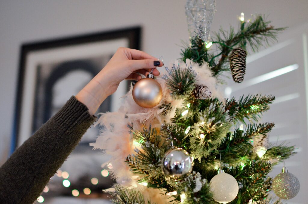 Person's hand shown as they put an ornament on their decorated tree